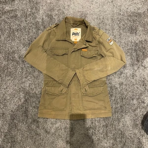 Superdry field jacket - En riktigt fet Field jacket från märket Superdry. Perfekt till våren/sommaren. Storlek S. Skick 6/10. En liten defekt - se sista bild. Skriv vid minsta fundering!😄