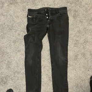 Svarta jeans från Diesel - Snygga svarta jeans från Diesel med knappgylf och klassisk femficksdesign. Jeansen har en diskret tvättad look och är perfekta för en stilren vardagsoutfit.