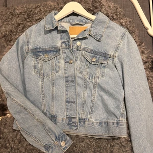 Ljusblå jeansjacka - Säljer en klassisk ljusblå jeansjacka med knappar framtill och två bröstfickor. Jackan har en normal passform och långa ärmar. Perfekt för vår och sommar! Aldrig använd, ifrån lager157
