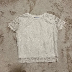 Vit spetsblus från FB Sister - Säljer en söt vit spetsblus från FB Sister i storlek XS. Blusen har korta ärmar och ett vackert blommigt spetsmönster. Perfekt för en somrig look!