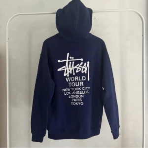 Mörkblå hoodie från Stussy - Säljer en mörkblå hoodie från Stussy med tryck av olika städer på både fram- och baksidan. Står att det är storlek S men skulle säga att det är M eller liten L!