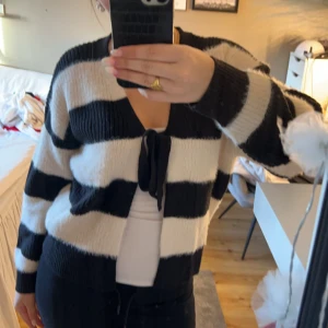 Randig kofta med knytband - Säljer en mysig svartvit randig kofta med knytband framtill. Koftan har långa ärmar och är perfekt för kyligare dagar. Passar bra till både jeans och kjol. Köpt nyss så den är i nyskick endast använd en gång 