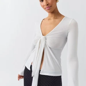 Vit knytblus från Gina Tricot - Säljer en stilren vit blus från Gina Tricot med knytning framtill. Blusen har långa ärmar och en djup v-ringning, perfekt för en chic look.