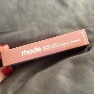 Rhode Peptide Lip Tint - Rhode Peptide Lip Tint i en söt rosa nyans. Denna läpprodukt kommer i en praktisk tub och är berikad med peptider för att ge näring och färg till läpparna. Perfekt för en naturlig look med en hint av färg. Oöppnad