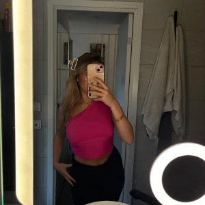 Rosa oneshoulder topp - Snygg rosa oneshoulder topp som är croppad och perfekt för en trendig look. Toppen har en tight passform och är tillverkad i ett mjukt material som sitter skönt mot huden.