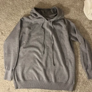 Grå hoodie - Helt ny alldrig använd då den inte passaSäljer en stilren grå hoodie med långa ärmar och justerbar huva. Perfekt för en avslappnad look. Ribbstickade muddar vid ärmslut och nederkant ger en skön passform.