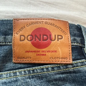 Blå jeans från Dondup - Säljer ett par snygga blå jeans från Dondup i japansk selvedge denim. De har en cool slitningseffekt och är tillverkade i Italien. Perfekta för en avslappnad stil med en touch av edge. Passar bra till både vardag och fest!