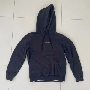 Mörkblå hoodie från Calvin Klein - Säljer en snygg och bekväm mörkblå hoodie från Calvin Klein. Den har en klassisk design med känguruficka och justerbar huva. Perfekt för kyliga dagar eller en avslappnad stil. Passar både till vardags och mysiga hemmakvällar.