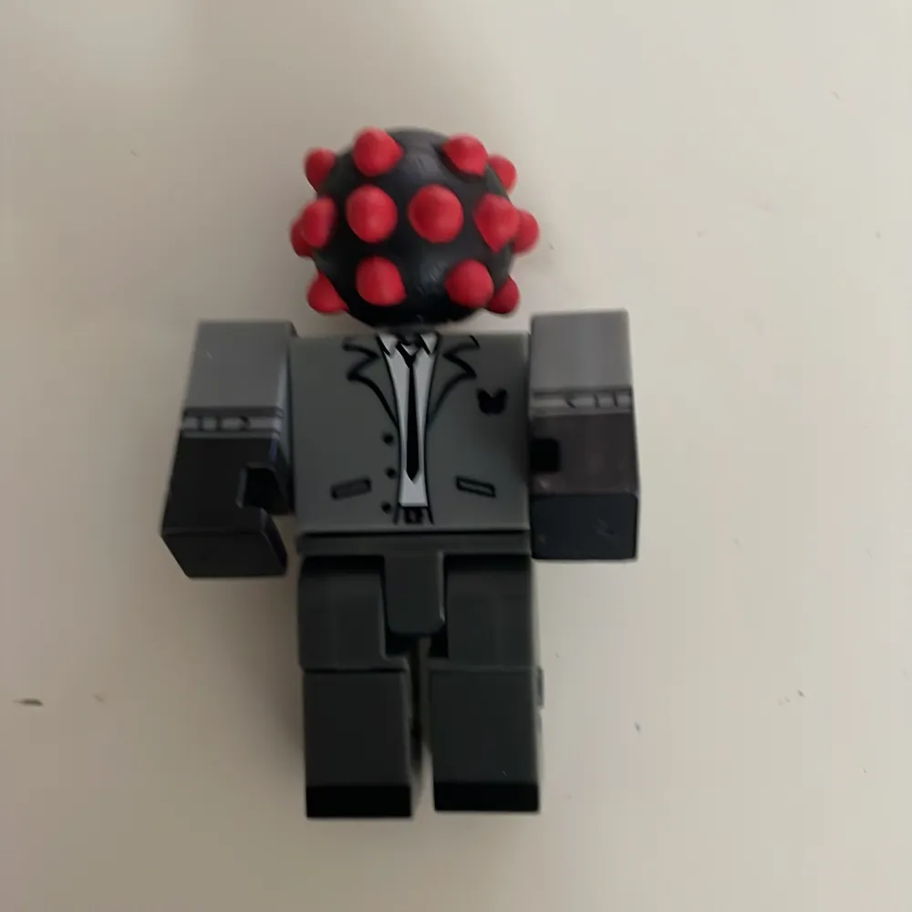 Cool Roblox-figur från Mystery Figure Series 10. Den har en unik design med ett grått kostymtryck och ett huvud som ser ut som en svart boll med röda prickar. Perfekt för samlare eller som en rolig leksak för . Övrigt.