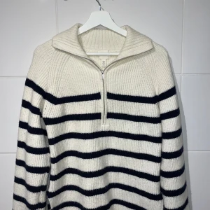 Randig stickad tröja med dragkedja - Säljer en supermysig stickad tröja från H&M i herrstorlek M. Den är vit med svarta ränder och har en praktisk dragkedja vid halsen. Perfekt för kyliga höst- och vinterdagar. Tröjan är i bra skick och redo för nya äventyr!