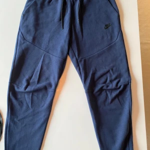Mörkblå mjukisbyxor från Nike - Säljer ett par mörkblå mjukisbyxor från Nike lite noppriga på rumpan (se bild 3) och en liten reva på vänster knä (se bild 4) även dessa har mitt namn stående på en lapp inuti. De är dock extremt bekväma och är perfekta för både träning och chill. Vid frågor är det bara att kontakta mig!