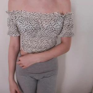 Prickig offshoulder topp - Säljer en superfin offshoulder topp med svartvita prickar. Den är croppad och har korta ärmar med volangdetaljer. Perfekt för sommardagar eller en festlig kväll. Toppen är i nyskick och passar perfekt till både jeans och kjol!