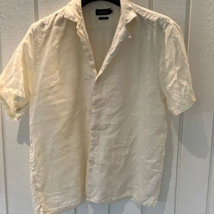 Beige linneskjorta från Riley - Säljer en stilren beige skjorta från Riley i storlek L. Skjortan är tillverkad i linne vilket gör den perfekt för varma sommardagar. Den har korta ärmar och knappar framtill. Perfekt för en avslappnad men ändå snygg look! Skick: nyskick
