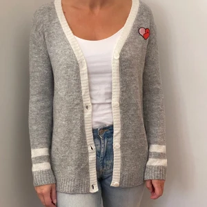 Grå kofta med hjärtdetalj från H&M - Mysig grå kofta från H&M med vita detaljer och ett sött hjärta på bröstet. Perfekt för höst och vinter! Den har långa ärmar och knappar framtill. Superfin att ha över en t-shirt eller linne. 🩶