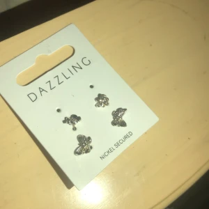 Söta örhängen från Dazzling - Säljer ett set med tre par örhängen från Dazzling. De är i silverfärg och har olika former, inklusive blommor och fjärilar. Perfekta för att ge en glittrig touch till din outfit! 🦋✨