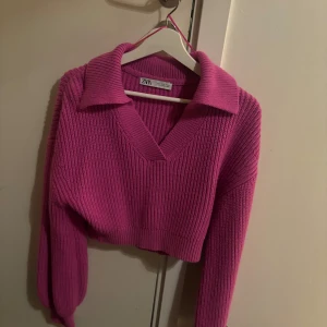 Rosa stickad tröja från Zara - Säljer en superfin rosa stickad tröja från Zara. Den har en snygg v-ringning och en krage som ger en stilren look. Perfekt för höst och vår! Tröjan är croppad och har långa ärmar, vilket gör den både trendig och bekväm. Passar perfekt till jeans eller kjol. 💖