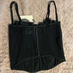 Svart korsett med spetsdetaljer - Snygg svart korsett med spetsdetaljer och justerbara axelband. Perfekt för en festlig kväll eller en speciell tillställning som halloween! Enbart testad, säljer då jag behöll i en blå färg. 