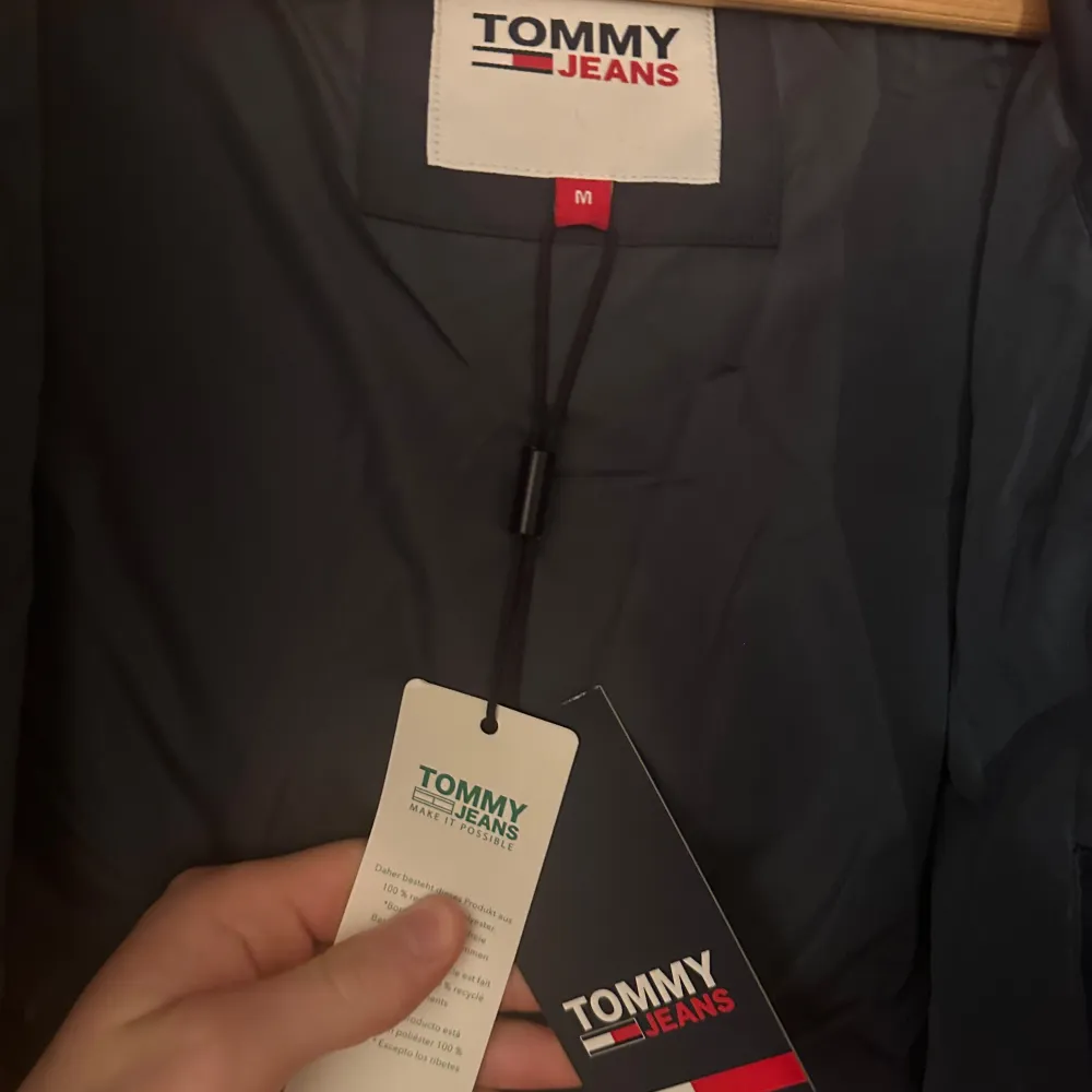 Blå puffer jacka från Tommy Hilfiger i storlek M. Helt ny/oanvänd med prislapp kvar och säljs på grund av att den aldrig kommit till användning. Fin passform och passar bra framåt kallare årstider. Luvan är avtagbar!. Jackor.