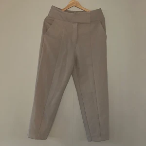 Beiga högmidjade chinos - Högmidjade, beige byxor i skönt material. Sömmar löper över benen. 