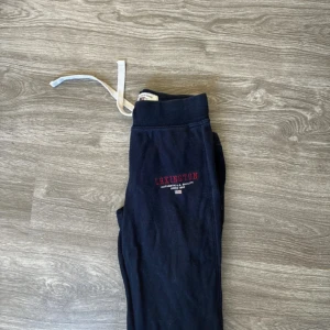 Svarta mjukisbyxor från Lexington - Säljer ett par svarta mjukisbyxor från Lexington i storlek XS. De är superbekväma med elastisk midja och dragsko för perfekt passform. Perfekta för en chill dag hemma eller en snabb tur till affären. Lexington-loggan är snyggt broderad i rött på sidan. Passa på att fynda dessa sköna byxor!