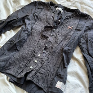 Odd Molly blus - Supersöt blus från odd Molly med knappar som stängning i fram. Små tygsnören som man knyter till rosett högst upp. Fint broderi och ett grått tyg.