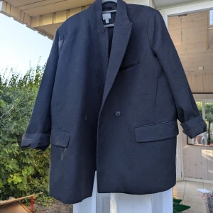 Svart kavaj från H&M - Säljer en stilren svart kavaj från H&M i storlek XXL. Kavajen har en klassisk design med två knappar framtill och fickor med lock. Perfekt för både formella och semi-formella tillfällen.Har endast provat, men lagat och samlat damm. Vänligen se bilder