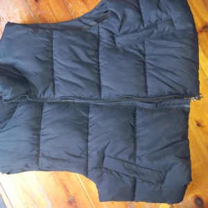 Svart väst från lager157 - Säljer en svart väst från lager157 i storlek XL. Västen har en dragkedja och knappar för extra säkerhet. Perfekt för höst och vinter, håller dig varm och bekväm. Den är i nyskick och redo för nya äventyr!