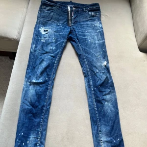 Dsquared2 Jeans - Säljer ett par snygga blå jeans från Dsquared2. De har en cool distressed look med slitningar och färgstänk. Perfekta för en avslappnad och trendig stil. Jeansen är i bra skick och har en normal passform. Storlek 46  Nypris ca 6000 kr 