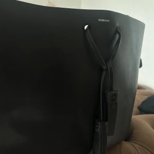 Svart axelväska från Pomikaki - Säljer en snygg och stilren svart läder axelväska från Pomikaki. Köpt i Italien för ca 1 år sedan för ca 750kr. Säljer den då den inte kommer till användning. Den rymmer väldigt mycket och är perfekt till skolan/jobbet.