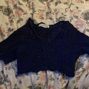 stickad bolero - En marinblå/lila stickad bolero med lite blomliknande detaljer framtill (stickat så det efterliknar blommor inte något mönster) bra skick och man kan stänga den genom ett spänne 💕
