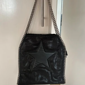 Stella McCartney liknande väska - Säljer denna svarta Stella McCartney liknande väska som jag köpt i Spanien. Super snygg med stjärna på framsidan🌟Som ny💕