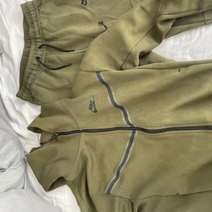 Olivgröna mjukisbyxor från Nike - Säljer ett par olivgröna mjukisbyxor från Nike. De har en bekväm passform med elastisk midja och snörning. Perfekta för avslappnade dagar eller träning. Byxorna har en diskret Nike-logga på sidan. Passar bra till höst och vår. 350 tröjan 400 med byxorna