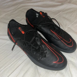 NIKE PHANTOM GT ELITE FG BLACK X CHILE RED - Ett par svart röda fotbollskor av märket Nike, använt någon enstaka gång. I topp skick utan några som helst fel. storlek 40, konstgräs/AG. Priset kan diskuteras