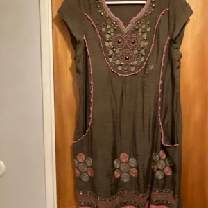 Grön klänning från Custo Barcelona - Säljer en unik grön klänning från Custo Barcelona med vackra broderade detaljer i rosa och grönt. Klänningen har korta ärmar och ett dekorativt mönster med paljetter och broderier. Perfekt för höst och vår, med en bohemisk touch. Passar både till vardags och festliga tillfällen. Storlek 38-40. S