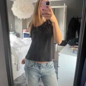 Volang topp - Säljer nu en jättefin volang topp som är one shoulder. Inga defekter alls! Köpt i spanien. Den är mörkgrå/svart 😁