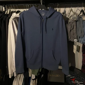 Ralph Lauren Zip - Säljer en snygg blå hoodie från Polo Ralph Lauren. Den har en dragkedja framtill och en klassisk logga på bröstet. Perfekt för en avslappnad stil. Hör av dig vid intresse!