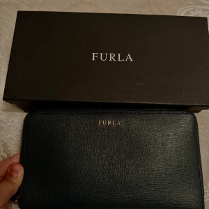Mörk grön  plånbok från Furla - Elegant grön plånbok från Furla med dragkedja runtom. Tillverkad i skinn med flera kortfack och en myntficka med dragkedja. Perfekt för att hålla ordning på dina kort och kontanter. Kommer i originalförpackning.