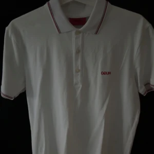 Vit pikétröja från Hugo Boss - Snygg vit pikétröja från Hugo Boss med röd logga på bröstet. Köpt för 1200 kr.