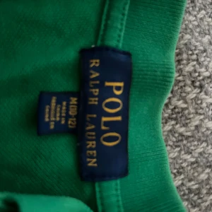 Grön pikétröja från Ralph Lauren - Säljer en snygg grön pikétröja från Ralph Lauren med klassisk krage och korta ärmar. Tröjan har en broderad logotyp på bröstet i blått. Perfekt för en stilren och avslappnad look.10-12år priset kan diskuteras vid snabb affär 