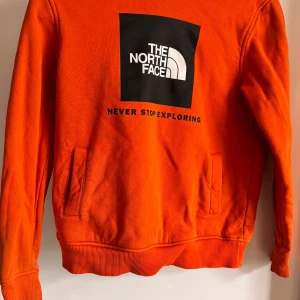 Orange tröja från The North Face - Säljer en cool orange tröja från The North Face med deras ikoniska logga på framsidan. Tröjan är tillverkad i 100% bomull. Två mindre fläckar som inte har gått bort i tvätten. Passar stl 152 