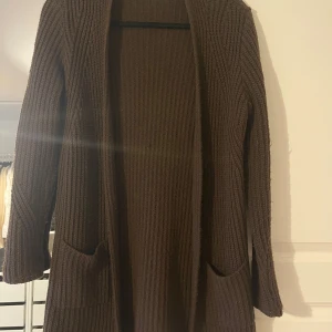 Brun stickad kofta från ASOS - Säljer en mysig brun stickad kofta från ASOS. Koftan har långa ärmar och praktiska fickor framtill. Kofta äään är lite nopprig därav lågt pris 