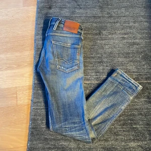 Blå jeans från Replay - Snygga blå jeans från Replay med slitna detaljer och en klassisk femficksdesign. De har en knappgylf och är i modellen Anbass. Perfekta för en avslappnad stil.