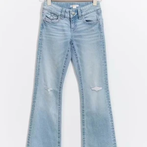 Ljusblå bootcut jeans från Gina Young - Snygga ljusblå bootcut jeans med slitna detaljer på knäna. De har en klassisk femficksdesign och en knappgylf. Perfekta för en avslappnad stil med en touch av vintagekänsla. Har också fickor där bak