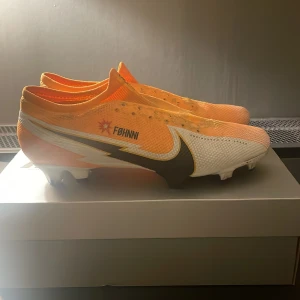  fotbollsskor - Snygga fotbollsskor från Nike i en fräsch gul och vit färgkombination. Skorna har en strömlinjeformad design med en stor Nike-logga på sidan. Perfekta för att dominera på planen med stil.