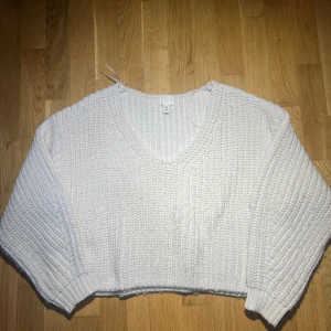Vit stickad tröja från H&M - Säljer en mysig vit stickad tröja från H&M. Tröjan har en v-ringad design och är croppad med långa ärmar. Perfekt för kyliga dagar när du vill vara både bekväm och stilren. Passar utmärkt till jeans eller kjol för en avslappnad look.