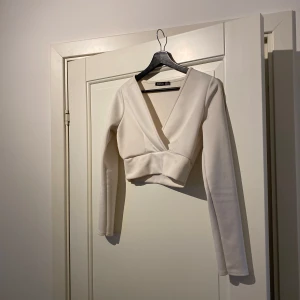 Vit omlottopp från Boohoo - Säljer en stilren vit omlottopp från Boohoo. Toppen har en djup v-ringning och långa ärmar, perfekt för en elegant look. Materialet är mjukt och bekvämt, vilket gör den idealisk för både vardag och fest.