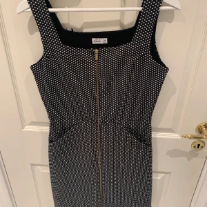 Svartvit prickig klänning från Robin - Snygg svartvit prickig klänning från Robin med dragkedja framtill. Klänningen är ärmlös och har en figurnära passform. Perfekt för en stilren look.