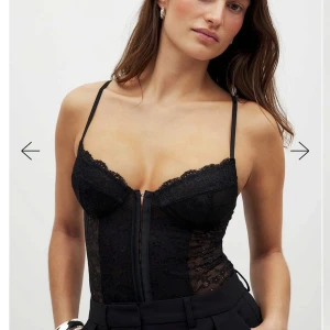 Svart spetskorsett - Snygg svart korsett i spets med smala. Den har en elegant design med genomskinliga spetsdetaljer och en åtsittande passform. Perfekt för att ge en stilfull touch till din outfit.