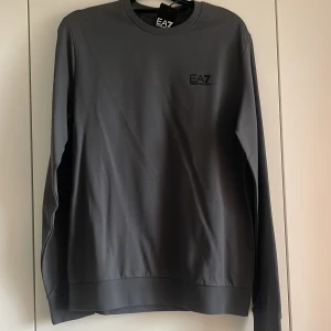 Grå sweatshirt från Emporio Armani EA7 - Snygg grå sweatshirt från Emporio Armani EA7 med rund hals och långa ärmar. Helt ny, prislappen är kvar!