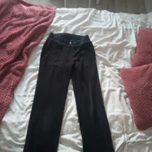 Svarta byxor från Juicy Couture - Snygga svarta byxor från Juicy Couture . Byxorna har dekorativa fickor med knappar baktill och en stilren design. Perfekta för en avslappnad men chic look.